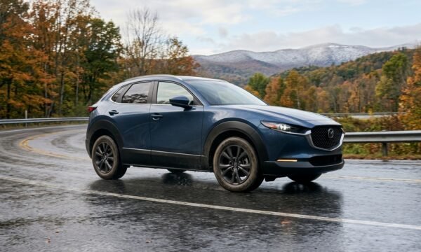 Featured Image Concept A premium automotive editorial scene showing a modern crossover equipped with all weather tires traveling on a wet road during changing seasonal conditions. The scene should communicate year round driving without exaggerating winter capability. Featured Image Prompt Create a realistic professional automotive editorial photograph, 1200 × 675 pixels, 16:9 aspect ratio. Show a modern crossover vehicle driving naturally on a wet paved road after rainfall, with subtle seasonal scenery in the background and a light amount of snow visible far in the distance. The tire area should be visible enough to communicate an all weather tire concept without displaying fake specifications. Use realistic natural lighting, authentic road reflections, detailed tire texture, premium automotive photography, clean composition, and a trustworthy editorial appearance. Do not include fake dashboards, fake product packaging, fake statistics, misleading performance claims, unnecessary text, fabricated documents, or random brand logos. The final image should look like an original professional photograph for an informational automotive article.